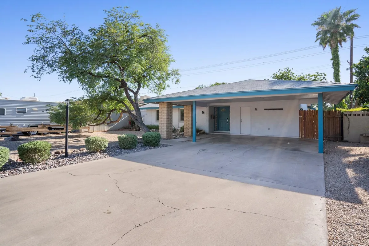 A wide exterior view of the home, featuring vibrant blue trim, green foliage, and a spacious driveway. The landscaping and open space evoke a welcoming, family-friendly vibe.