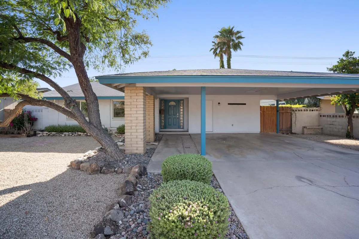 A welcoming exterior scene with a green front door, landscaped garden, and carport. The front porch area hints at opportunities for morning coffee and casual outdoor gatherings, setting a friendly and inviting tone for arrivals.