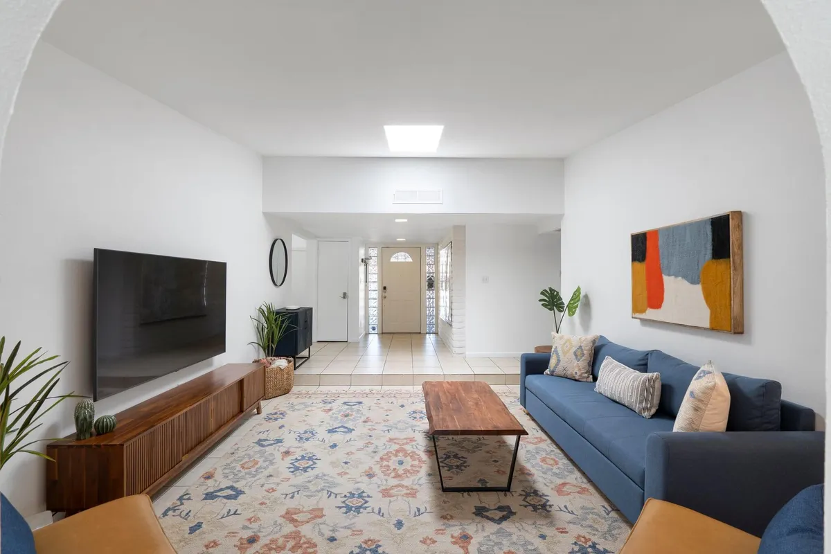 An inviting living area featuring a comfortable sofa, coffee table, stylish artwork, television, and visible entrance. The arrangement encourages both relaxation and entertaining guests, highlighting a versatile environment for family or friends.