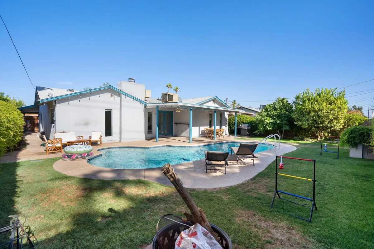 A vibrant exterior shot showcasing a swimming pool, outdoor seating, lush greenery, a play area, and a fire pit. The scene feels lively and cheerful, ideal for families with kids.