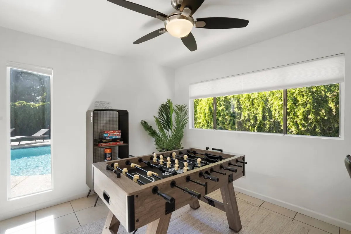An interior scene with a foosball table set by windows that provide a view of the pool and greenery outside. The space feels lively and fun, suggesting group activities, friendly competition, and easy flow between indoor and outdoor spaces.