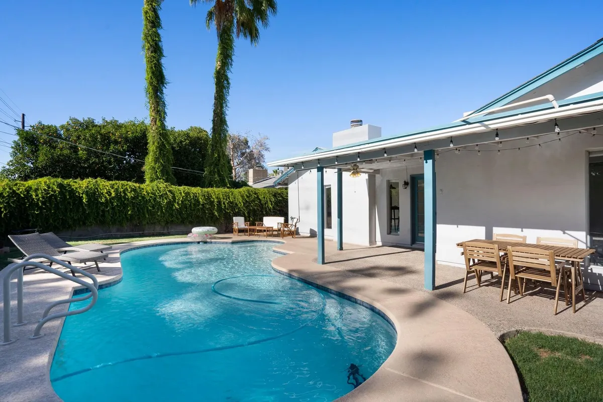 A cheerful outdoor scene showing a spacious swimming pool, lounge chairs, palm trees, and a stylish outdoor dining table set up for meals. The area is ideal for swimming, sunbathing, or enjoying alfresco dining with friends and family.