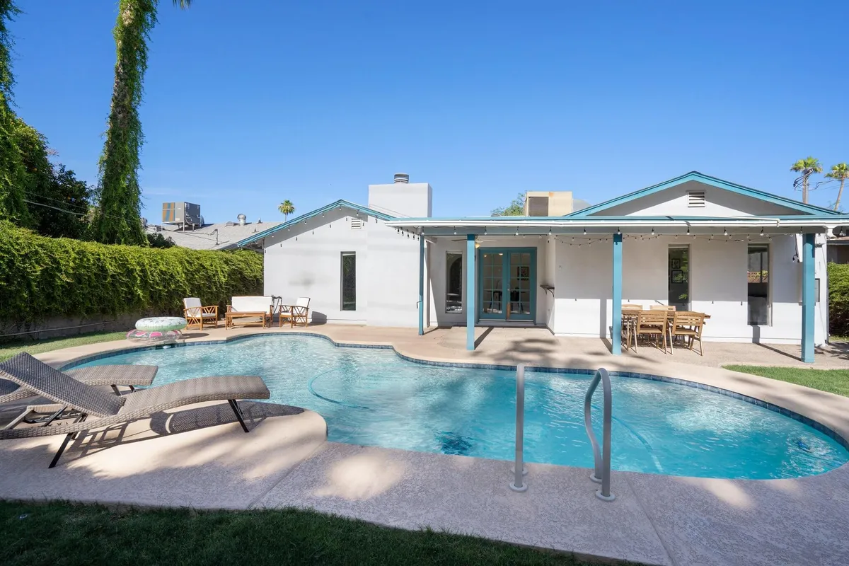 A spacious outdoor area featuring a swimming pool surrounded by lush greenery and an inviting outdoor seating area. The setup suggests a perfect spot for swimming, sunbathing, outdoor dining, or relaxing with friends, all under the Arizona sun.