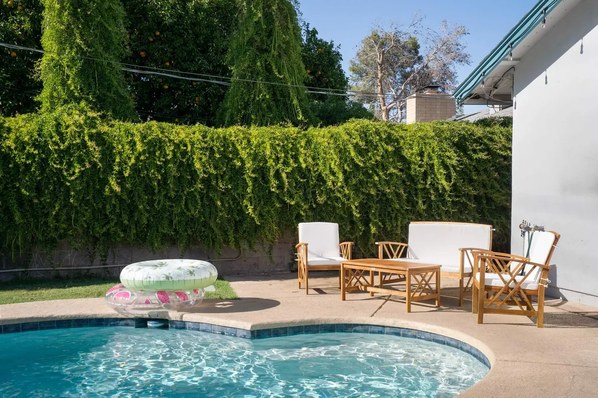 A tranquil backyard view at sunset, highlighting a serene swimming pool with adjacent outdoor seating. Lush greenery frames the setting, creating a private oasis perfect for relaxing, sunbathing, or hosting friends as the day transitions into evening.