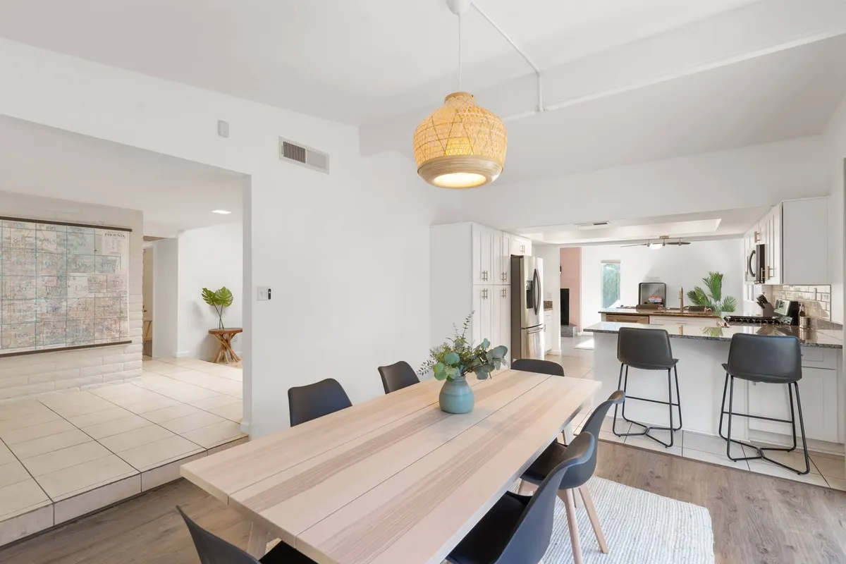 A spacious dining area with a large table, woven pendant light, kitchen in the background, and map artwork enhancing the space. The setting captures a vibrant zone ideal for family meals, social gatherings, and group activities.