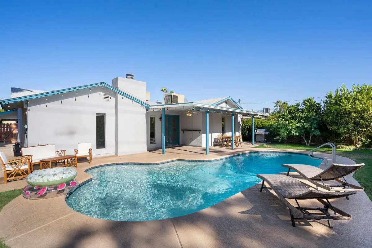 A vibrant backyard scene featuring a sparkling private swimming pool surrounded by lounge chairs and a cozy outdoor seating area, all set against lush, green landscaping. The space is clearly designed for both relaxation and social gatherings, with ample room for sunbathing or enjoying a poolside meal.