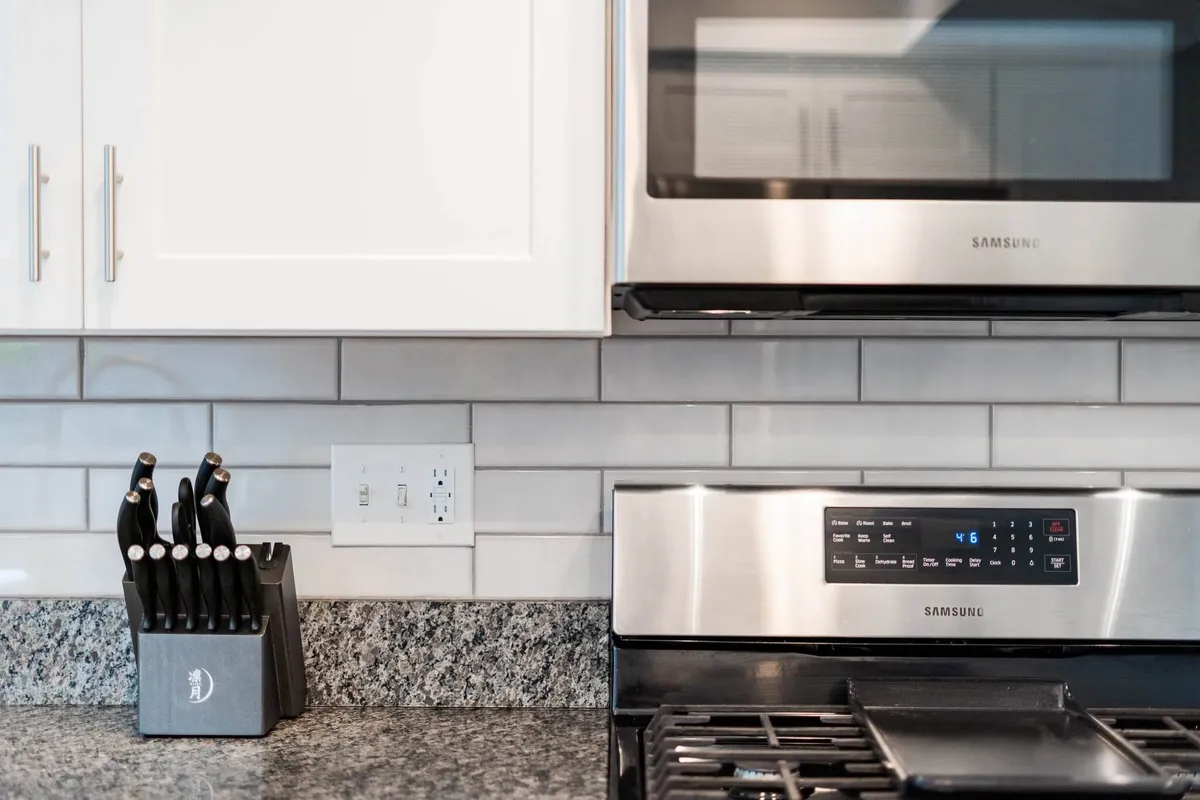 A stylish kitchen with kitchen knives on display, stainless steel appliances, granite countertop, and a clean subway tile backsplash. The setup suggests readiness for culinary creativity and communal meal preparation.