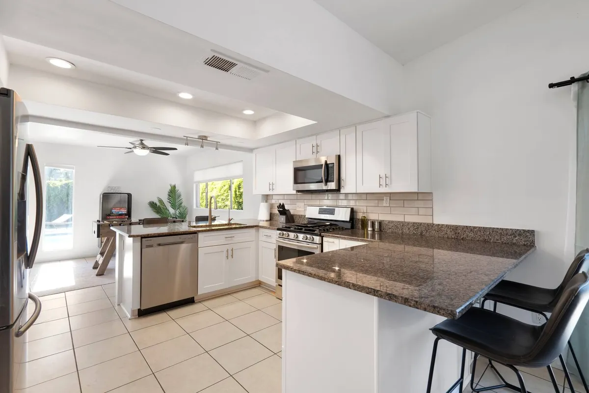 A bright, spacious kitchen with granite countertops, stainless steel appliances, white cabinetry, and an open layout. The kitchen island and wide counters invite group cooking, and there's plenty of space for multiple people to move around comfortably.